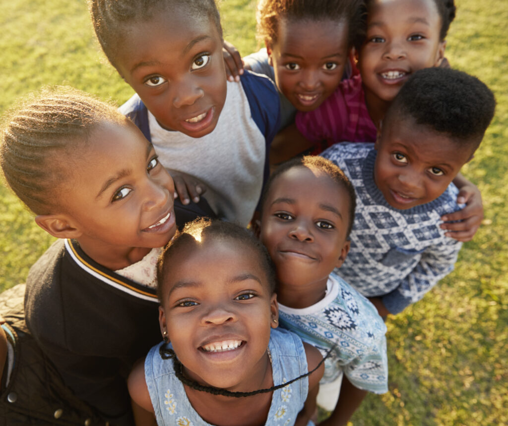 Elementary school kids in a field look up at  camera smiling