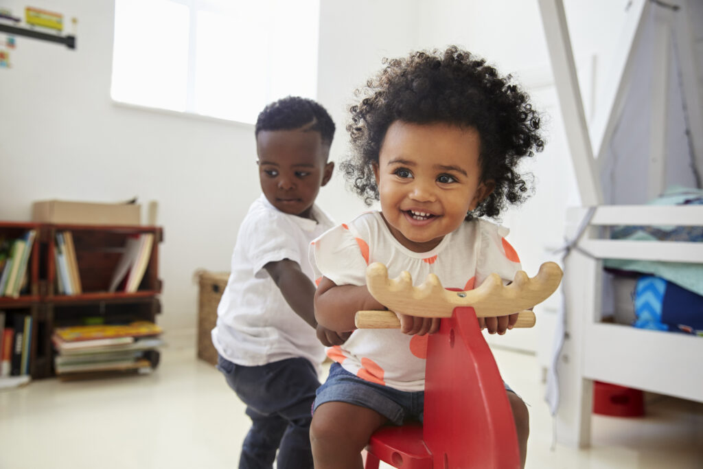 two-children-sitting-on-ride-on-toy-in-playroom